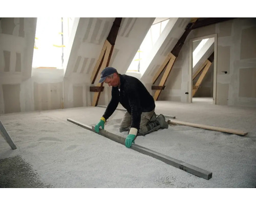 Ambachtsman egaliseert egalisatiekorrels op een zolder met een rechte lat.