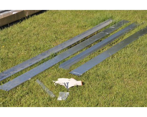 Verschillende metalen profielen, een pak schroeven en een handschoen liggen op het gras.