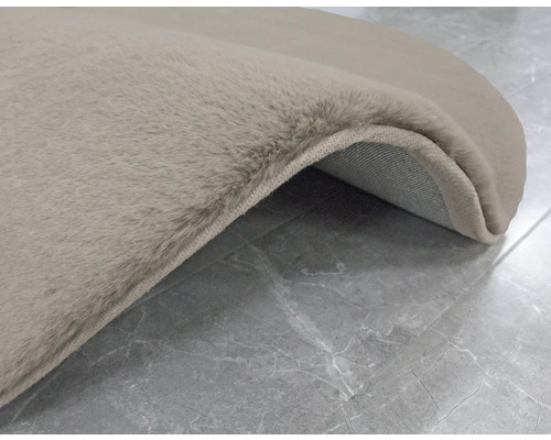 Detail van een beige vloerkleed met hoogpolig oppervlak op een betegelde vloer.