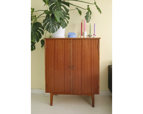 Houten kast met twee deuren en vier poten, versierd met een kamerplant en kaarsen