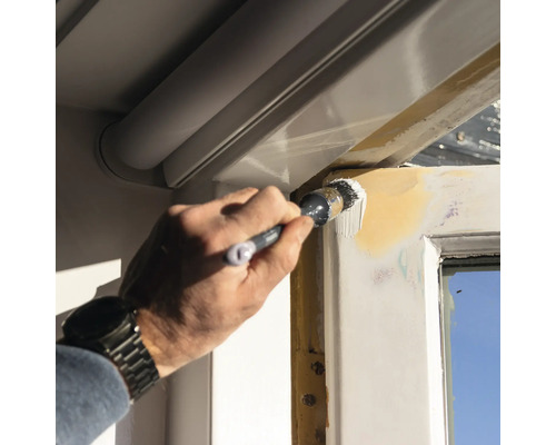 Een persoon schildert een raamkozijn met een penseel.