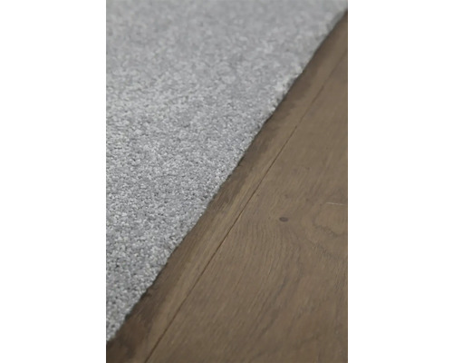 Detailopname van een lichtgekleurd tapijt op een houten vloer.