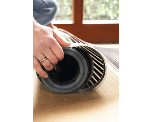 Een persoon rolt een elektrische vloerverwarmingsmat uit.