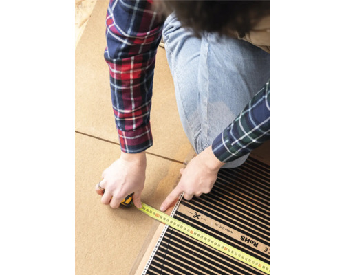 Iemand meet een elektrische vloerverwarmingsmat met een meetlint.