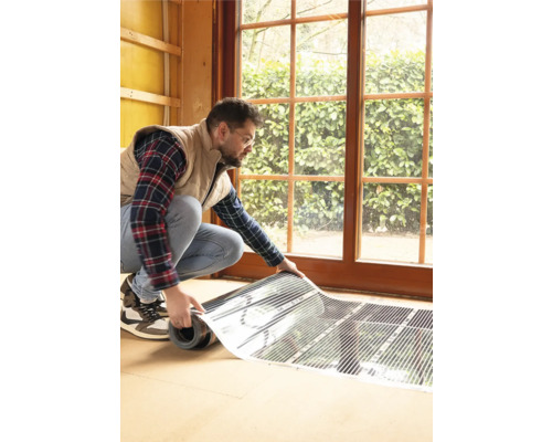 Een man installeert elektrische vloerverwarming in een kamer met een raam.