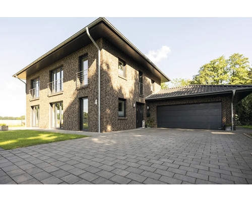 Een bakstenen huis van twee verdiepingen met garage en bestrate oprit