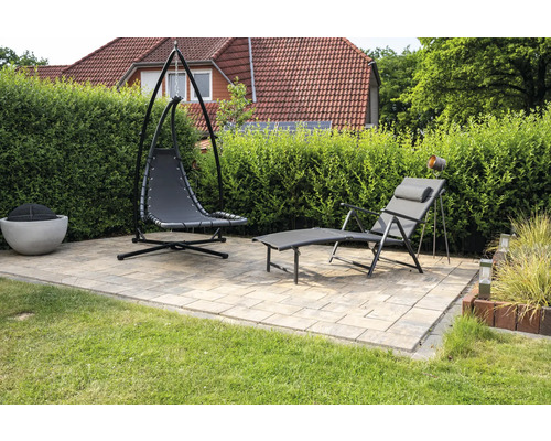 Tuinscene met hangstoel, ligstoel en vuurplaats op een betegeld terras