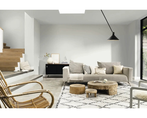 Lichte woonkamer met bank, houten salontafel, vloerkleed en trap.