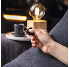 Een persoon bedient een afstandsbediening in een woonkamer met een lamp en een kopje.