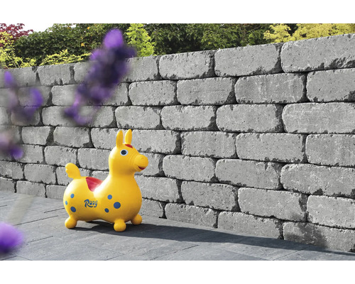 Gestapelde grijze betonstenen vormen een tuinmuur met een kinderspeelgoed ervoor.