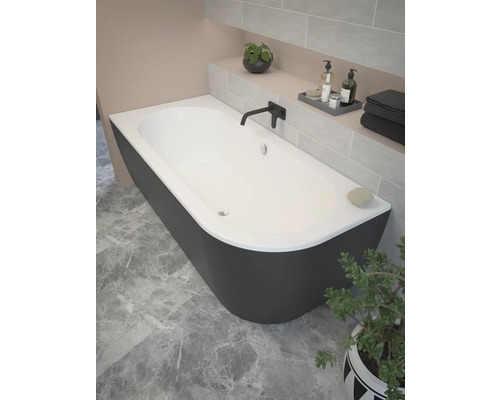 Vrijstaand bad in een badkamer met betegelde muur en plant