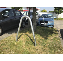 Twee metalen fietsenrekken op een groenstrook tussen geparkeerde auto''s.
