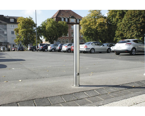 Roestvrijstalen bolder op een parkeerplaats met geparkeerde auto''s.