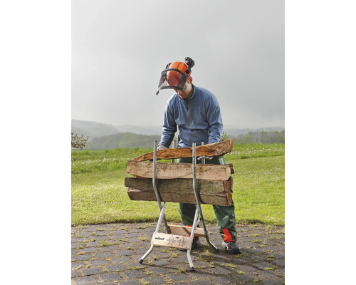 Een man met veiligheidshelm en vizier werkt met een houtklover waarop houtblokken liggen.