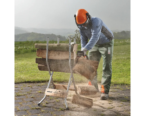 Een persoon zaagt met een kettingzaag hout op een zaagbok in de buitenlucht.