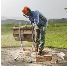 Een persoon gebruikt een houtzaagbok om houtstammen te zagen in een buitenomgeving.