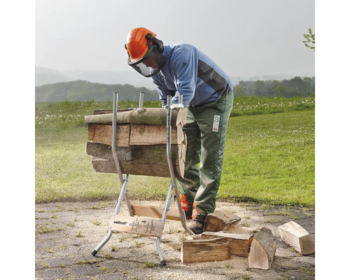 Een persoon gebruikt een houtzaagbok om houtstammen te zagen in een buitenomgeving.