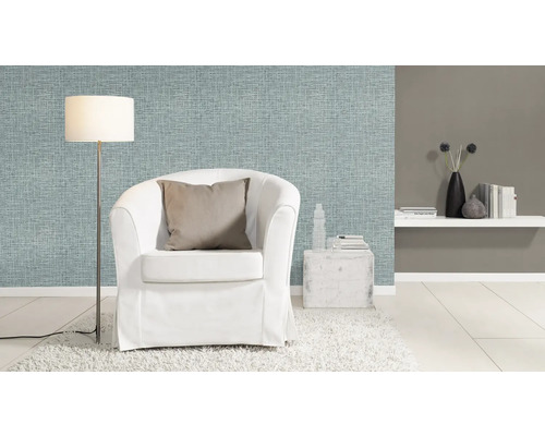 Woonkamer met lichtblauw textielbehang, witte fauteuil en vloerlamp.