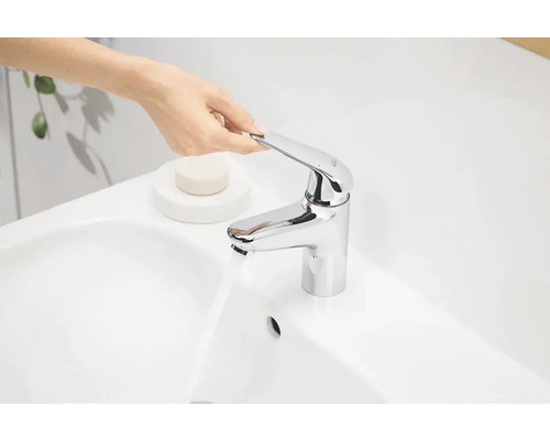 Persoon bedient een verchroomde kraan op een witte wastafel