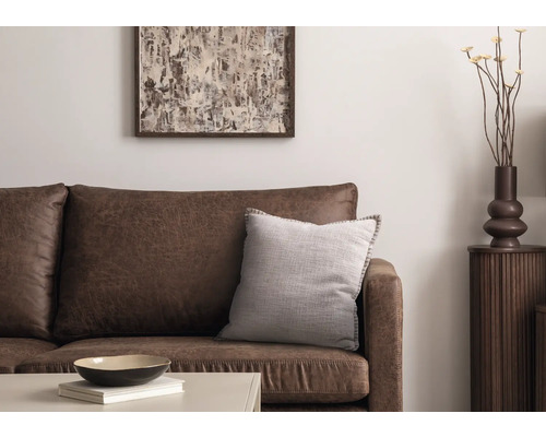 Woonkamerscène met bruine leren bank, decoratief kussen, tafel, decoratie en kunstwerk