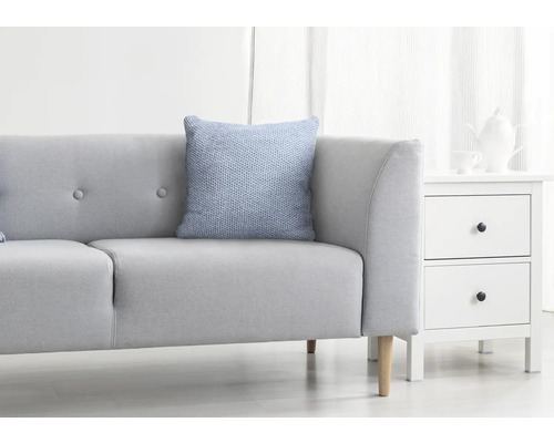 Lichte woonkamer met grijze bank, blauw kussen en wit nachtkastje