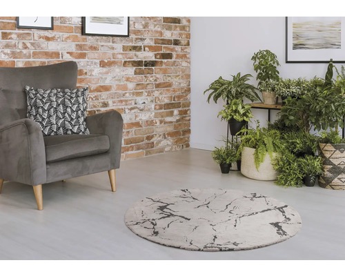 Woonkamer met grijze fauteuil, rond tapijt en kamerplanten voor een bakstenen muur.