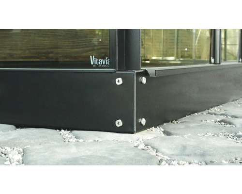 Detail van een metalen kasframe met schroeven op een stenen vloer. Vitavia Logo.