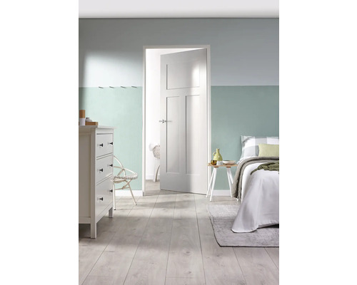 Lichte slaapkamer met commode, bed en openstaande witte binnendeur