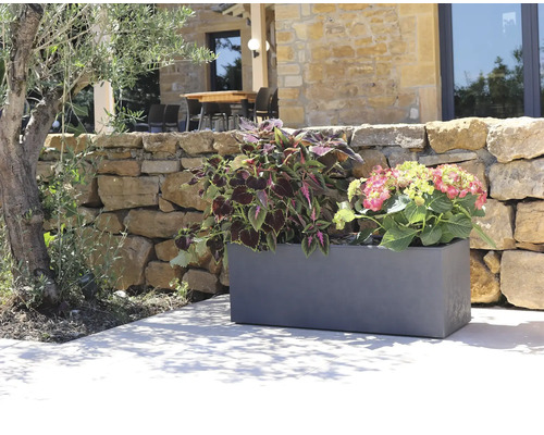 Kunststof plantenbak met planten voor een stenen muur