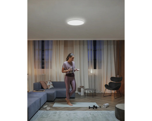 Een vrouw staat op een yogamat in een woonkamer met een ronde plafondlamp.