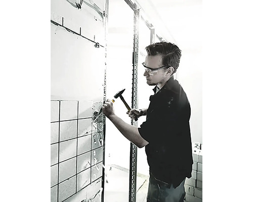 Een man gebruikt een hamer en beitel om tegels van een muur te verwijderen.