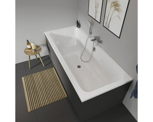 Scene van een badkamer met een rechthoekig bad met kraan, een kruk en een houten mat