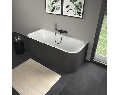 Vrijstaand bad met zwarte kraan in een badkamer met kunstwerken en een vloerkleed.