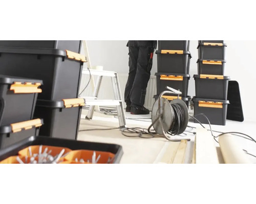 Foto van zwarte opbergdozen, een ladder en een elektricien aan het werk