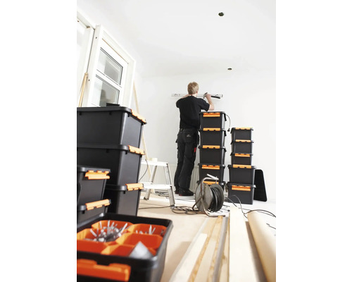 Een vakman werkt in een kamer met gereedschapskisten, een ladder en bouwmaterialen.