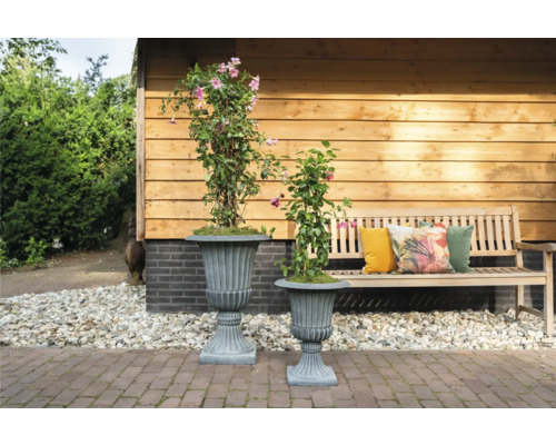 Twee plantenbakken met planten op een terras naast een houten bank.