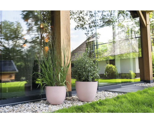 Twee ronde plantenbakken met planten op een grindpad voor een modern huis met een glazen gevel