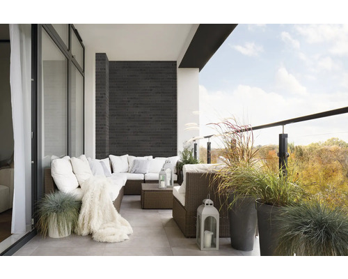 Balkon met rotan bank, kussens, deken, lantaarns en siergrassen in potten.