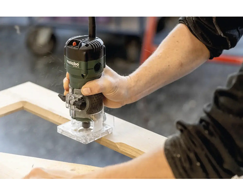 Een persoon gebruikt een Metabo bovenfrees op een houten frame.