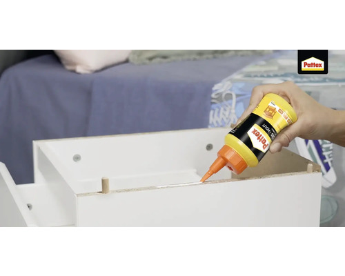 Een hand brengt een fles Pattex houtlijm aan op een wit meubelstuk