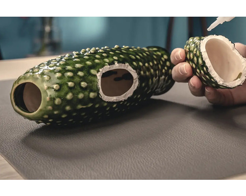 Decoratieve groene keramische schuilplaats voor vissen wordt gerepareerd met lijm.