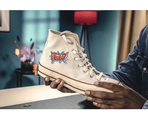 Persoon houdt een hoge sneaker met POW-patch in de hand