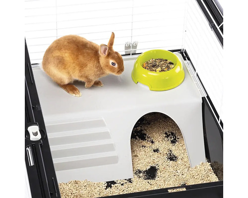 Klein konijn in een kooi met voerbak en schuilplaats