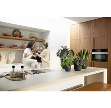 Lichte keuken met twee vrouwen, keukengerei, planten in potten en houten keukenkasten.
