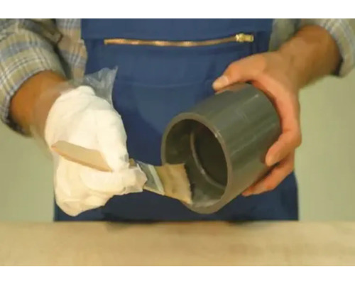 Een persoon brengt lijm aan op een kunststof buis met een borstel.