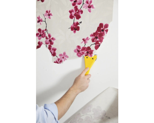 Behang verwijderen met een plamuurmes van een muur met een bloemmotief