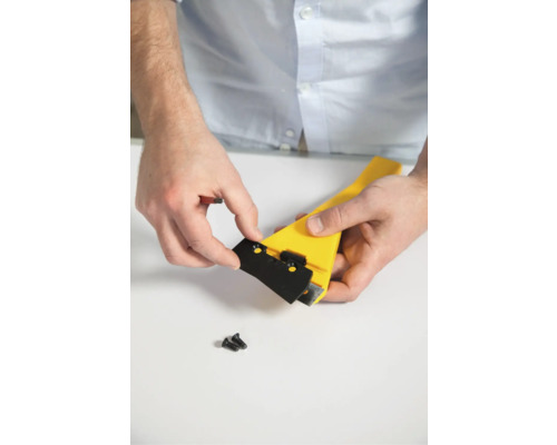 Een persoon bevestigt een zwart mes aan een gele schraper.