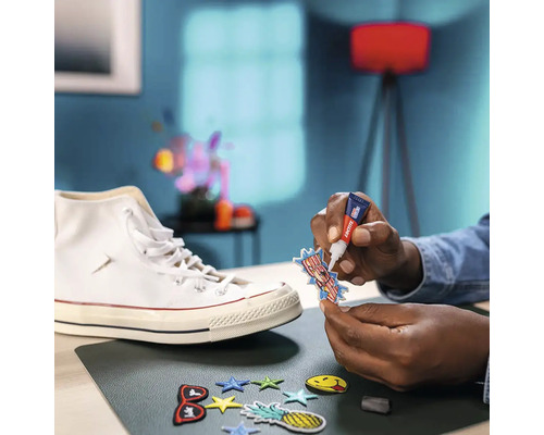 Een persoon bevestigt met lijm een embleem op een sneaker, omringd door andere emblemen op een tafel.