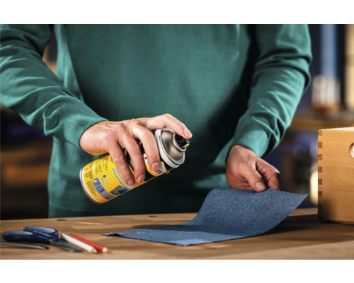 Iemand spuit lijm uit een spuitbus op een stuk stof om te lijmen.