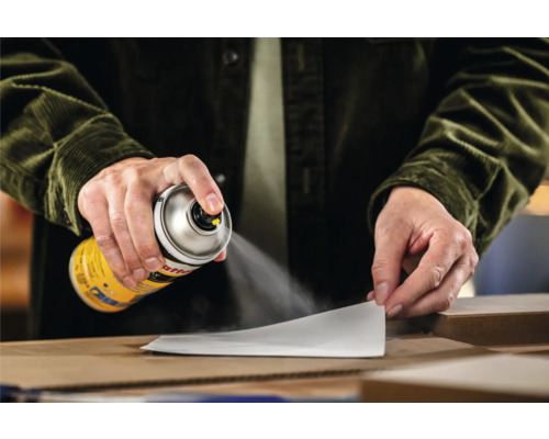 Een persoon spuit een spuitbus verf op een stuk papier.